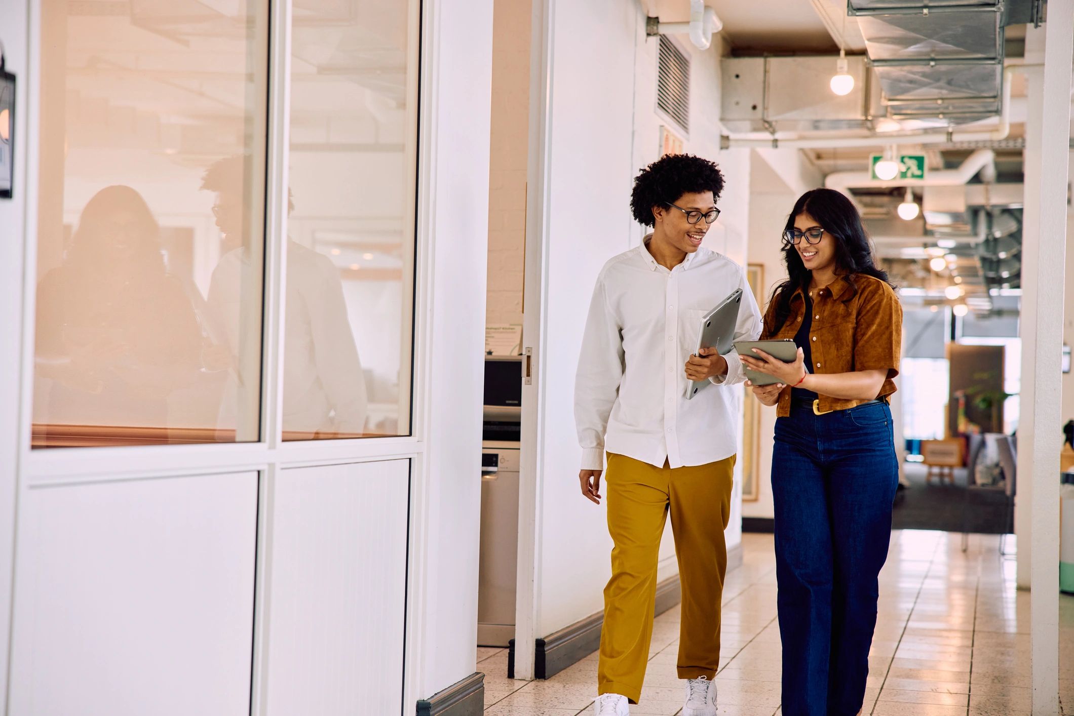 Two business colleagues discussing a tablet in an office corridor